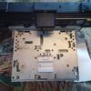 A printer is sitting on the floor with its front cover removed.