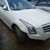 A white car parked in the mud with its front end broken.