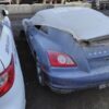 A blue car with the hood up in an alley.
