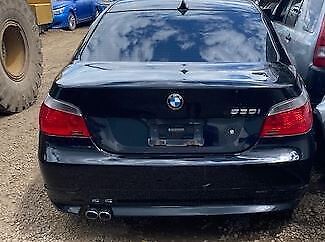 A black bmw parked in the dirt with two cars.