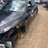 A black car that has been smashed in the middle of the road.