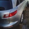 A silver car parked in the rain with its rear lights on.