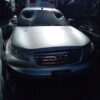 A silver car parked in the dark with people around.