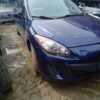 A blue car parked in the mud of a parking lot.