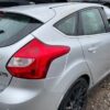 A silver car parked in the dirt with its rear lights on.