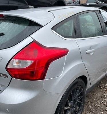 A silver car parked in the dirt with its rear lights on.
