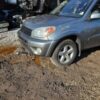A silver car parked in the dirt near some trees.