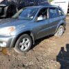 A silver suv parked in the dirt near some other vehicles.
