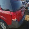 A red car parked in the grass with graffiti on it.