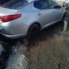 A silver car parked in the mud near some water.